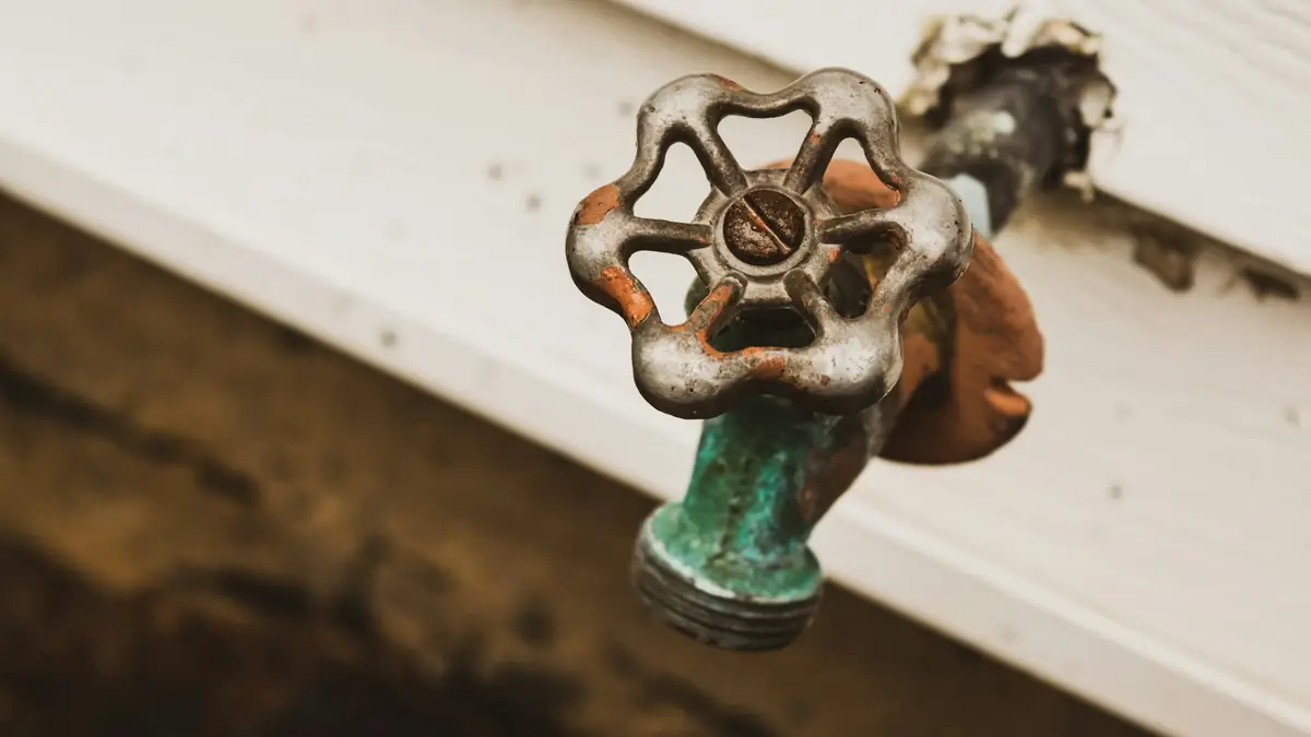 A rusty outdoor spigot with a round handle on white siding - Leak Detection in Cherry Hill